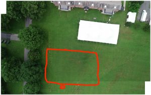 Drone photo from above of the site of the future Community Garden. Red rectangle where the garden will go, above that is a white rectangle, which is a tent for reunions, and above that is the Poker Flats apartments themselves.