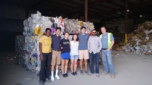 Group stands smiling in front of recycling