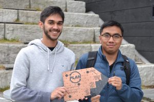Photo of two people smiling and holding a Bronze-colored plaque on an upcycled circuit board that says "PLAN"