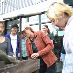 Six smiling people watch old-fashioned apple cider pressing