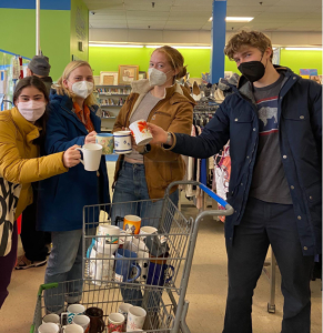 Four students stand over a shopping cart full of reusable mugs. Each holds a mug to the center of the photo. 