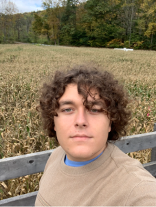 Student with curly brown hair takes stoic selfie in front of cornfield