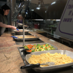 Serving line in dining hall with a dish of rice and one of colorful vegetables 
