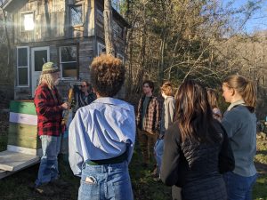 Man in flannel shirt demonstrates beekeeping skills to a group of students