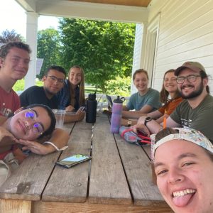 Interns smile and make silly faces while sitting at a long picnic table