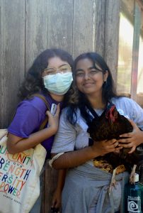Two students smile while one holds a large brown chicken