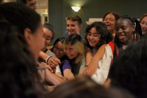 Students laugh as they put their hands in the center of a circle