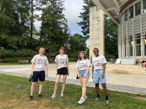 Four students wearing shirts that say "Compost Friends" pose smiling on lawn outside Paresky