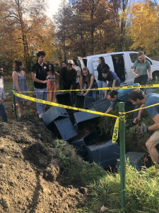 Students dump bins of soil into pit surrounded by caution tape