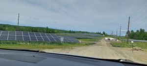 Rows of solar photovoltaic panels and associated infrastructure on gently rolling agricultural lands.