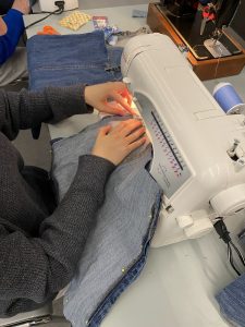 Hands guiding a piece of denim through a sewing machine