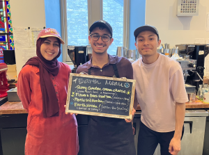 Three Goodrich Baristas stand smiling and holding the earth day menu board