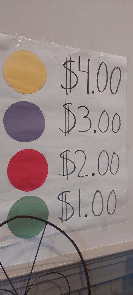 Sign with stickers indicating prices ($1, $2, $3, $4) at the Tag Sale