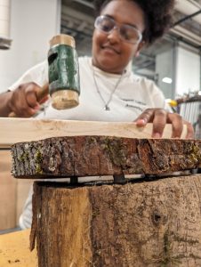 person wearing safety goggled hammers a piece of wood