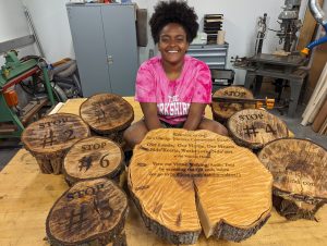 Yoyo sits in a bright pink shirt surrounded by her engraved wood cookies