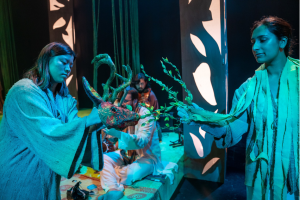 People in blue lighting hold a deer head with antlers and a laurel wreath