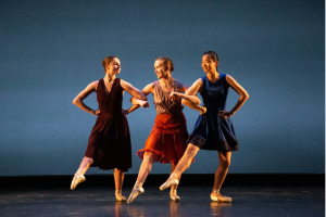 Three ballet dancers in summer dresses link arms and smile