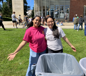 Two smiling student leaders serving as "Compost Friends" stand on Paresky lawn behind bins of compost.