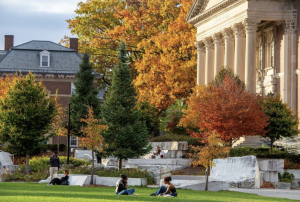 Bright orange trees and green pines stand in front of Chapin columns while students study on the lawn