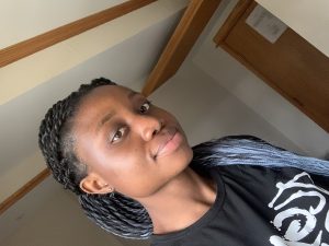 A selfie of a woman in braids wearing a black t-shirt. The selfie is askew to the left.