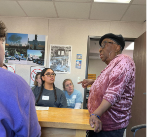 Woman in pink shirt and black hat talks to a group of students