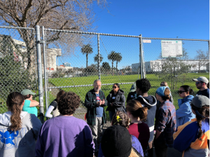 Group of students stands next to a fence and field during an outdoor field trip
