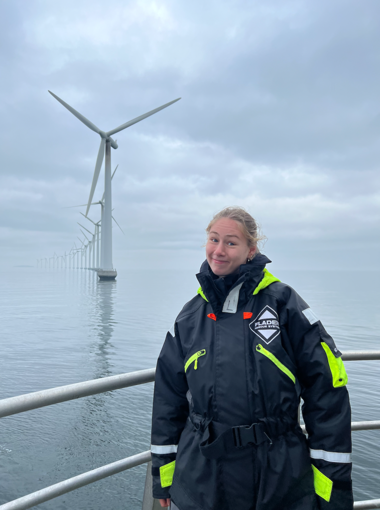 woman next to wind turbine. it is a cloudy day and the wind turbine is in the ocean