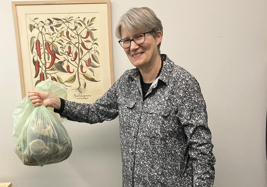 Woman with short grey hair stands smiling and holding a green bag of compost